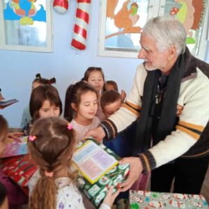 Older man handing out a christmas box to a group of little girls