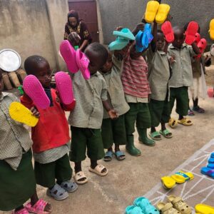 Small children standing in a line holding up bright colored shoes