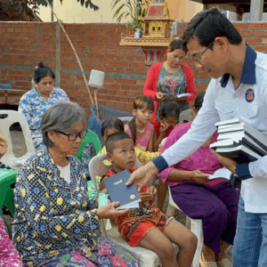 Man handing out Bibles to elderly lady sitting in a chair outside