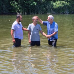 three men standing in water, praying over the man in the middle