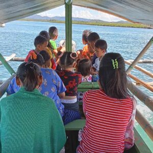 children and women sitting facing forward on a boat